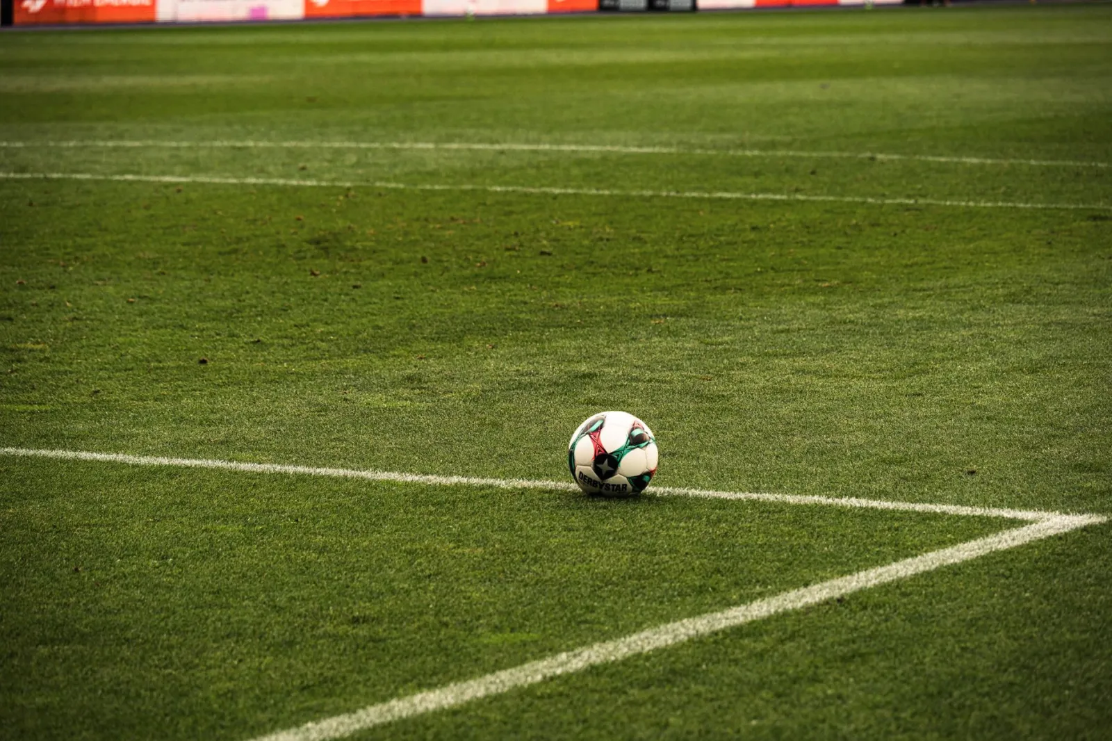 A soccer ball rests on a well-maintained green football field corner, ready for play.